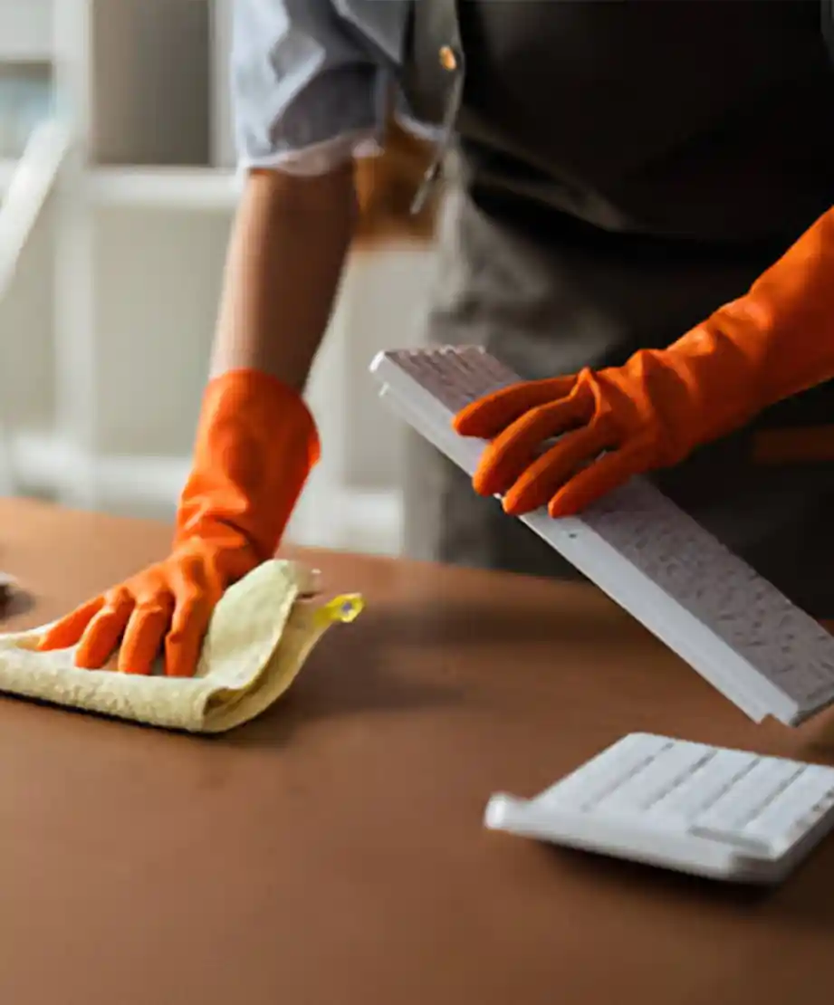 Reinigungsexperte mit orangefarbenen Handschuhen und Mikrofasertuch bei der Reinigung eines Schreibtisches