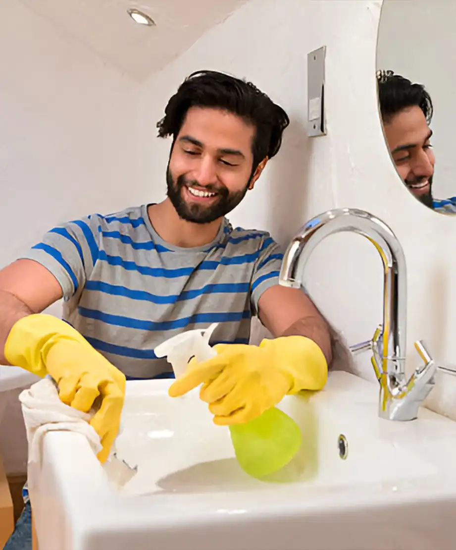 Mann beim Reinigen eines Waschbeckens mit Handschuhen und Reinigungsspray