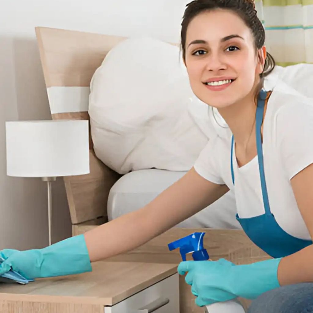 Smiling woman in a cap cleaning a surface with a spray bottle and cloth