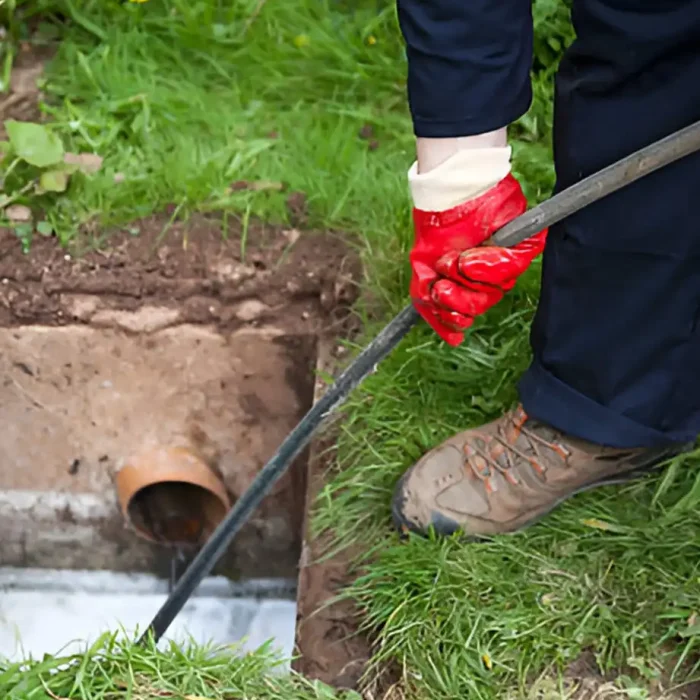 Arbeiter benutzt eine Stange, um einen verstopften Abfluss im Freien zu reinigen