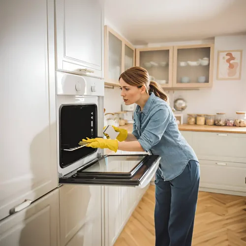 Frauen mit gelben Handschuhen und einem Schwamm beim Reinigen des Ofens in einem Bausatz
