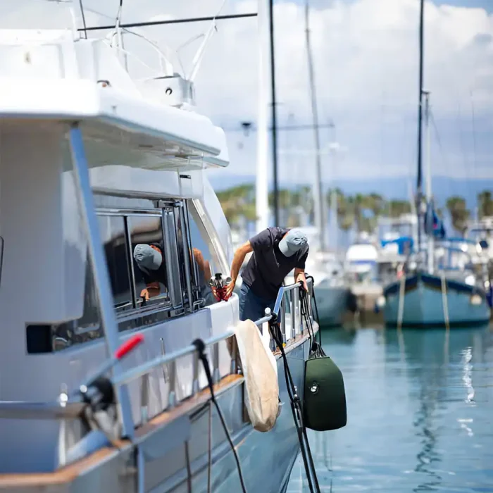Person, die ein Boot reinigt, während es in einem Yachthafen angedockt ist, mit anderen Booten im Hintergrund