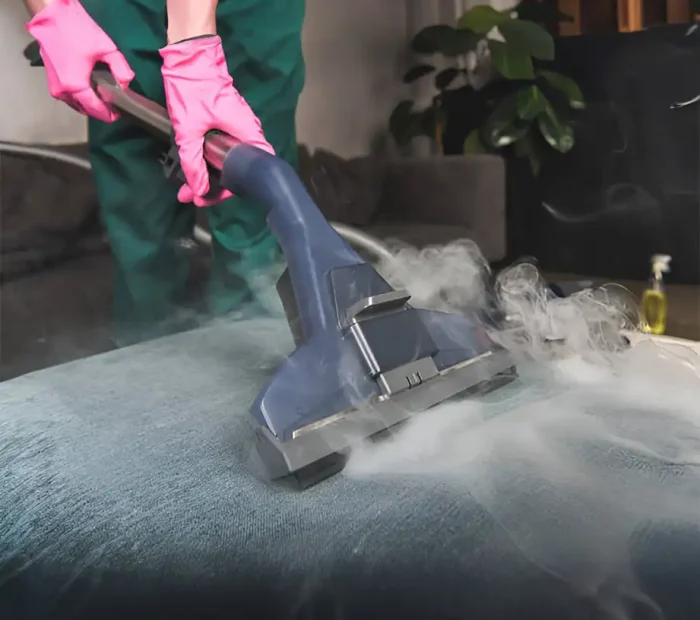 Frau mit rosafarbenen Handschuhen bei der Verwendung einer Dampfmaschine zur Feinreinigung eines Sofas