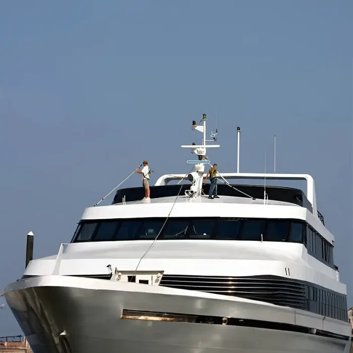 Zwei Menschen reinigen das Deck einer großen Yacht unter einem klaren Himmel