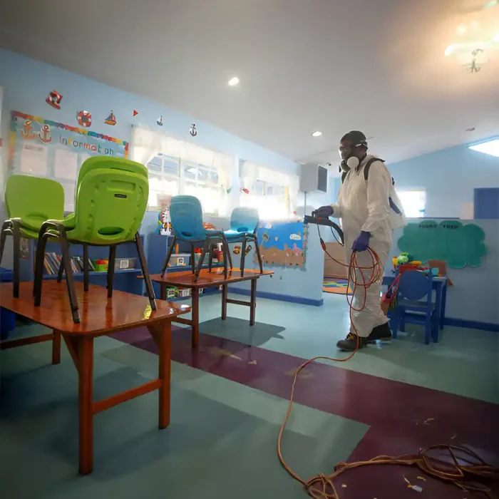 Techniker in Schutzkleidung bei der Desinfektion eines Kinderklassenzimmers