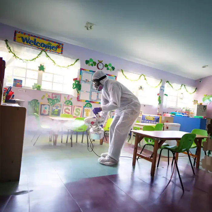 Ein Arbeiter in Schutzkleidung vernebelt einen bunten Vorschulraum