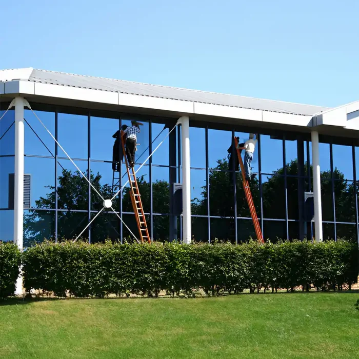 Arbeiter auf Leitern reinigen die hohe Glasfassade eines Gebäudes in Betzdorf