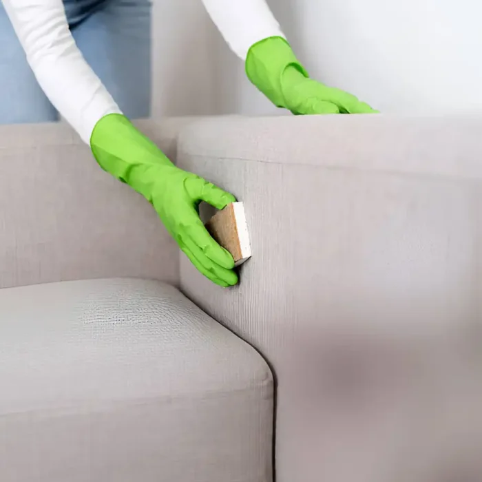 Person mit grünen Handschuhen, die ein Sofa mit einer Bürste bearbeitet in Guetersloh