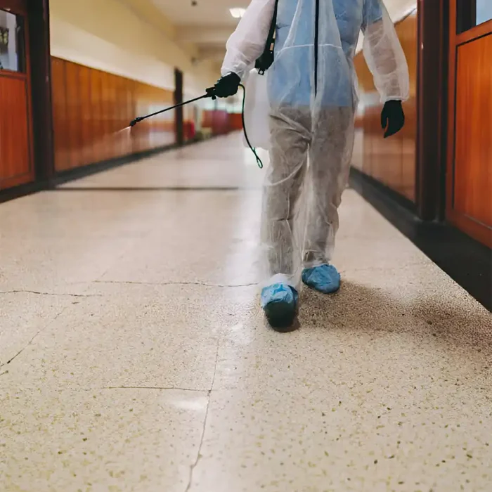 Arbeiter im Schutzanzug sprüht Desinfektionsmittel in einem Schulflur in Reutlingen
