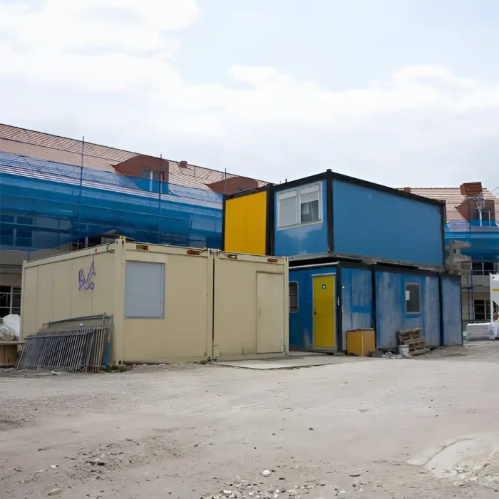 Zwei gestapelte und nebeneinander liegende modulare Einheiten in den Farben Blau und Gelb, die sich auf einer Baustelle mit Baumaterialien und Gerüsten befinden in Sinsheim