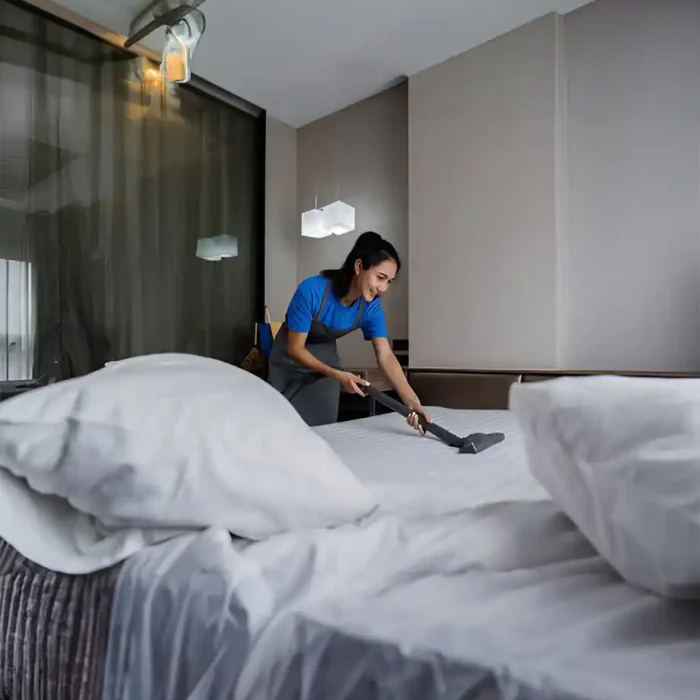 Eine Haushälterin benutzt einen Staubsauger auf einem Bett in einem modernen Hotelzimmer mit so