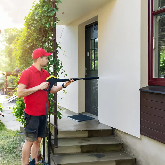 Person in rotem Outfit beim Hochdruckreinigen eines Hauseingangs