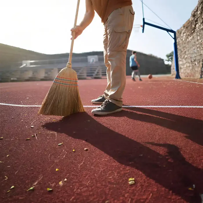 Person, die einen roten Basketballplatz im Freien mit einem großen Besen kehrt in Reutlingen