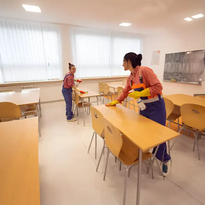 Zwei Arbeiter reinigen Schreibtische in einem hellen Klassenzimmer mit gelben Handschuhen in Reutlingen