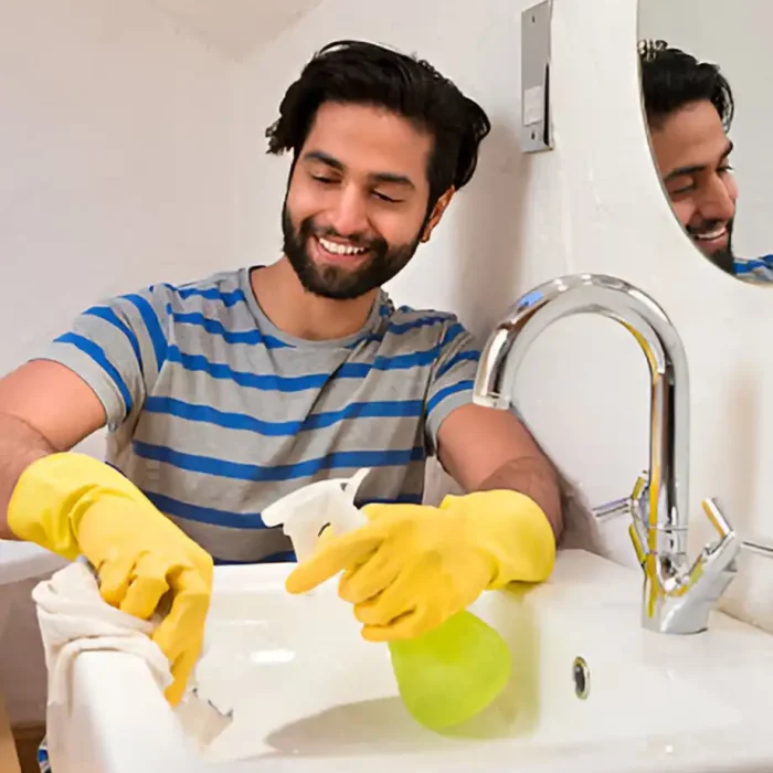 Mann beim Reinigen eines Waschbeckens mit Handschuhen und Reinigungsspray in Ludwigslust