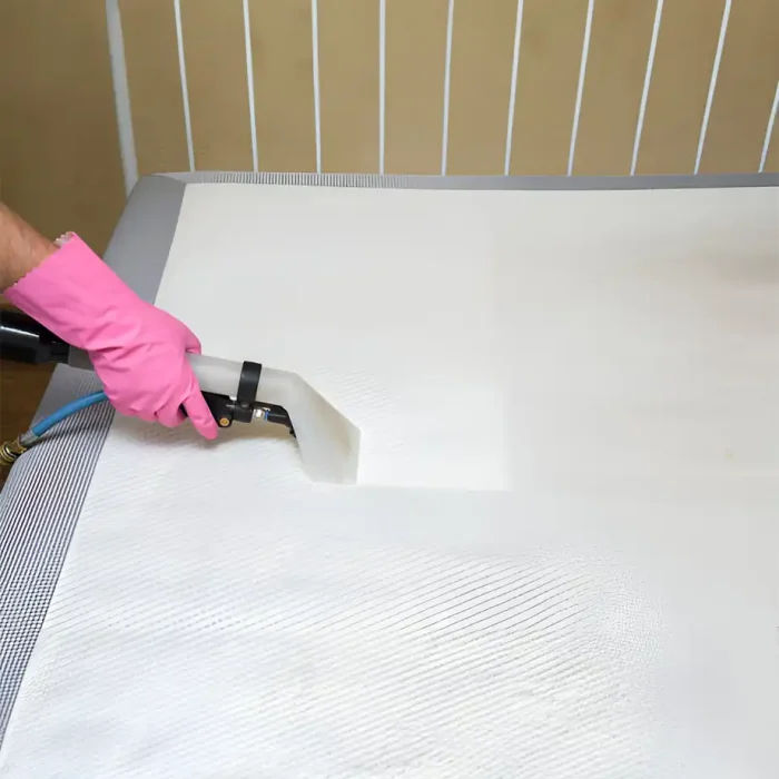 Person, die die Matratze staubsaugt, mit rosa Handschuhen und einem Staubsauger in der Hand in Lampertheim