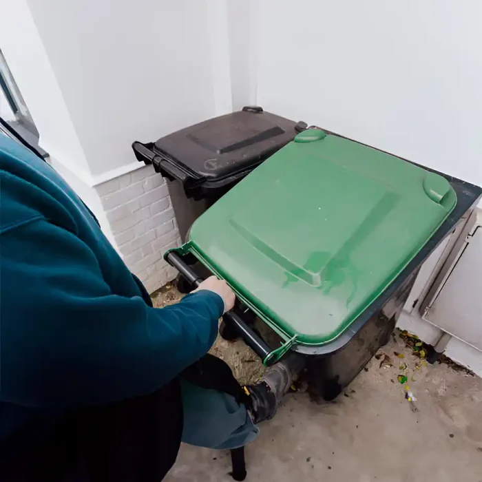 Einzelperson, die grüne und schwarze Mülleimer neben einem weißen Gebäude bewegt