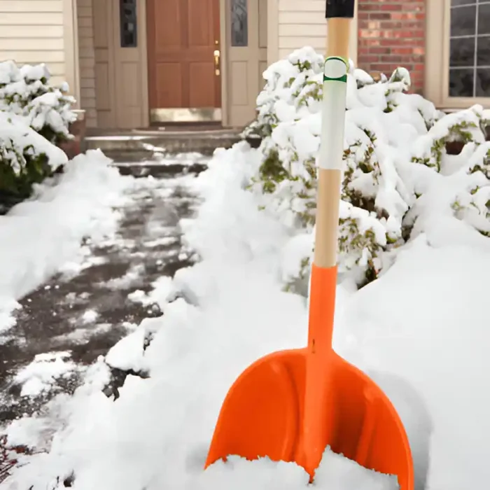 Leuchtend orangefarbene Schaufel steht im Schnee am Eingang eines Hauses