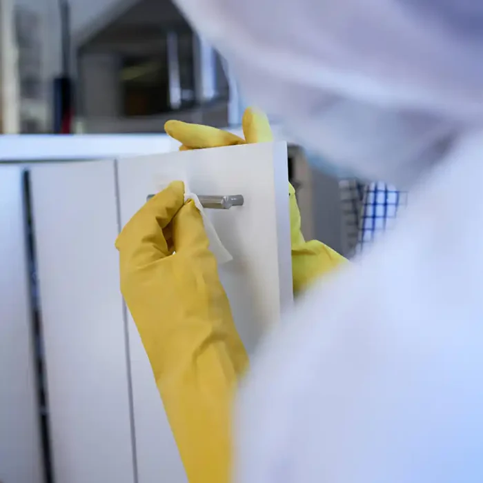 Person mit gelben Handschuhen, die einen Schrankgriff mit einem Tuch reinigt
