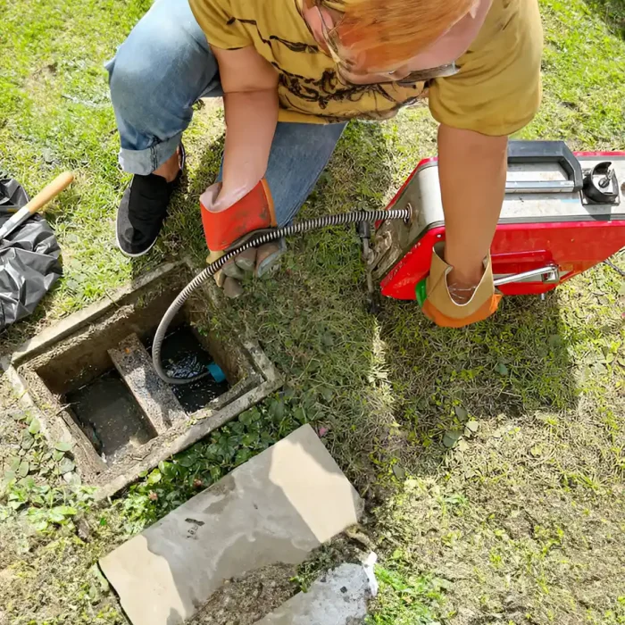 Person, die ein mechanisches Werkzeug benutzt, um einen Abfluss im Freien zu befreien