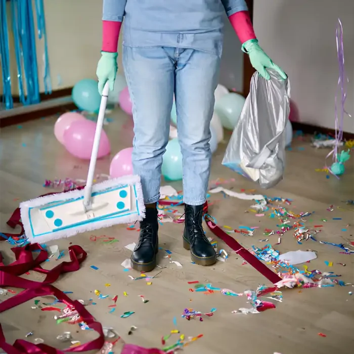 Person mit Handschuhen, Mopp und Müllsack beim Aufräumen nach einer Party in Coswig