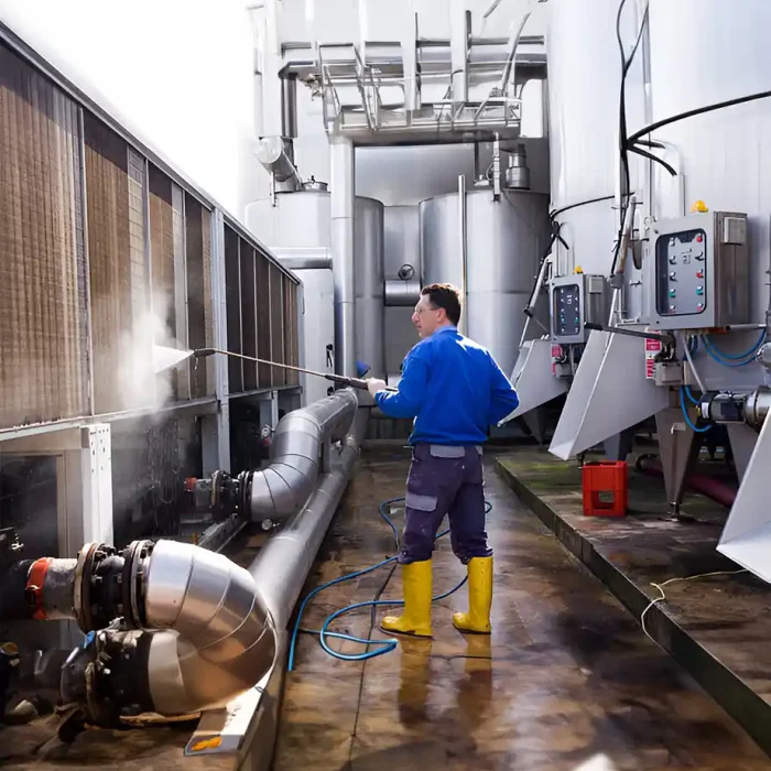 Arbeiter, der im Freien Industrieanlagen mit gelben Stiefeln druckwäscht in Recklinghausen