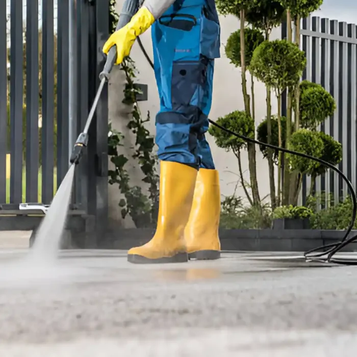 Arbeiter in gelben Stiefeln beim Hochdruckreinigen einer Betonoberfläche in der Nähe eines Tores