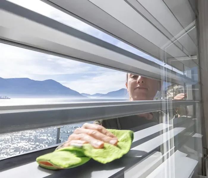 Frau hält ein Mikrofasertuch beim Reinigen eines Fensters mit üppigem Hintergrund