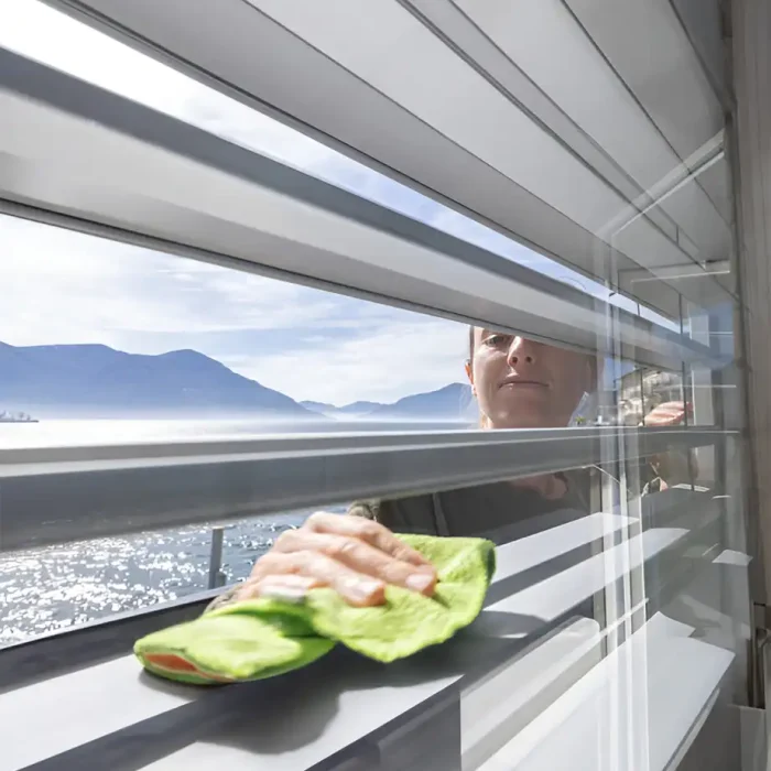 Frau hält ein Mikrofasertuch beim Reinigen eines Fensters mit üppigem Hintergrund