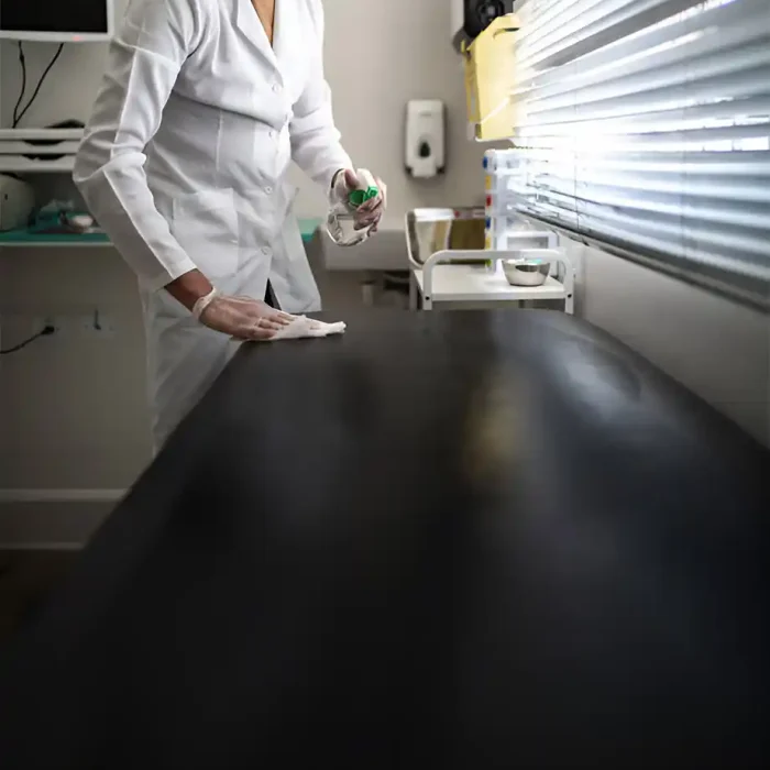 Person in Schutzkleidung und mit Maske reinigt eine schwarze Arbeitsplatte mit einem Spray und einem Tuch in einem medizinischen Umfeld in Friedberg