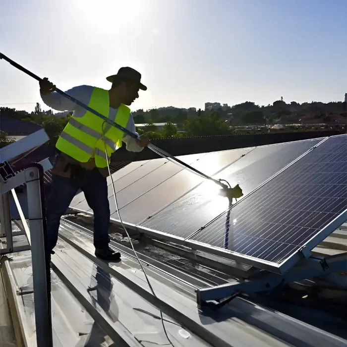 Arbeiter in Warnweste bei der Reinigung von Solarmodulen auf einem Metalldach