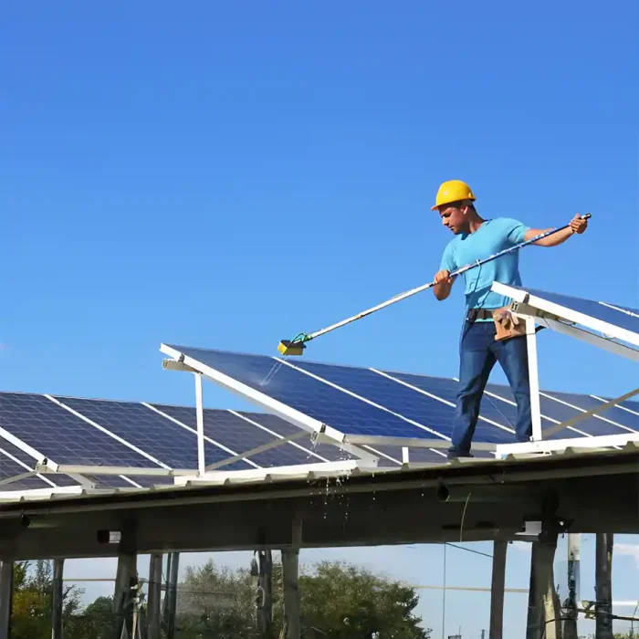 Ein Arbeiter reinigt mit einem langen Werkzeug Solarmodule auf einer Anhöhe