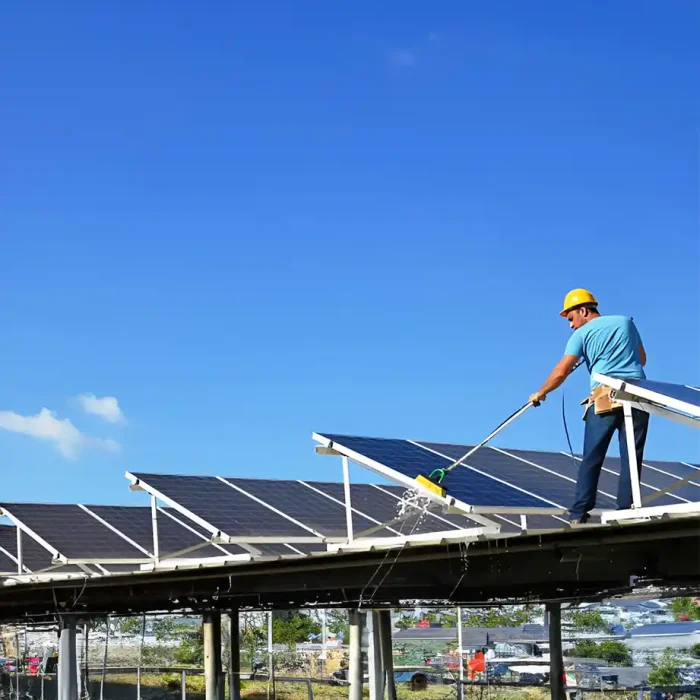 Arbeiter verwendet eine lange Bürste, um Solarmodule auf einer erhöhten Plattform zu reinigen