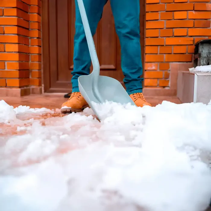 Nahaufnahme einer Person, die eine Schaufel benutzt, um Schnee von einer Veranda zu räumen