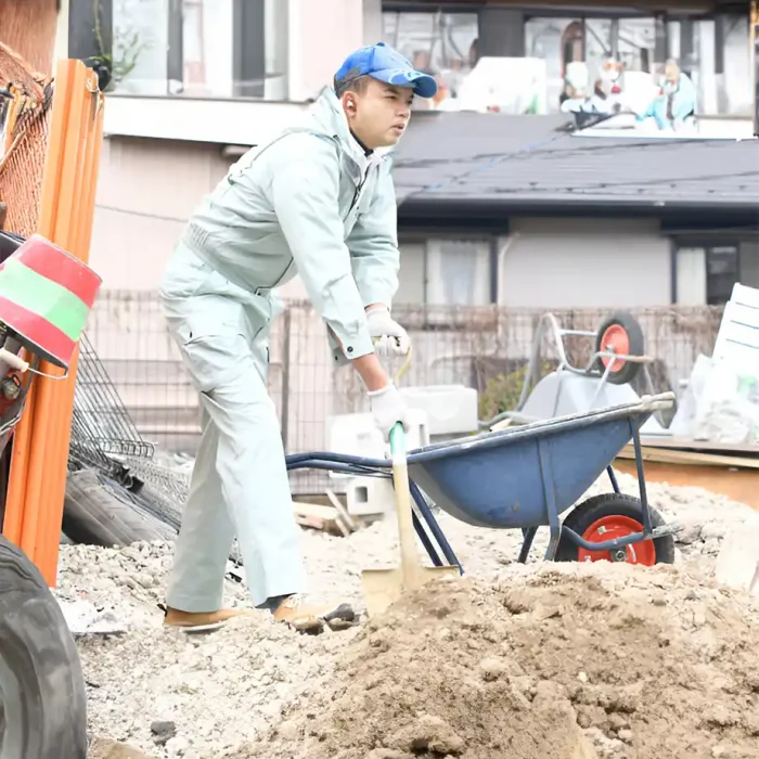 Ein Arbeiter in hellblauer Uniform schaufelt auf einer Baustelle Erde in eine Schubkarre in Sinsheim