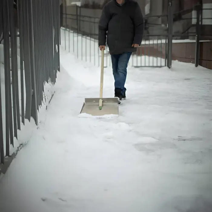Mann mit einer großen Schaufel auf einem schneebedeckten Bürgersteig