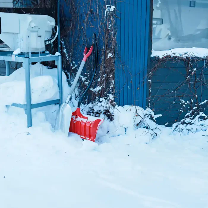 Rote und silberne Schneeschaufeln lehnen an einem verschneiten blauen Gebäude
