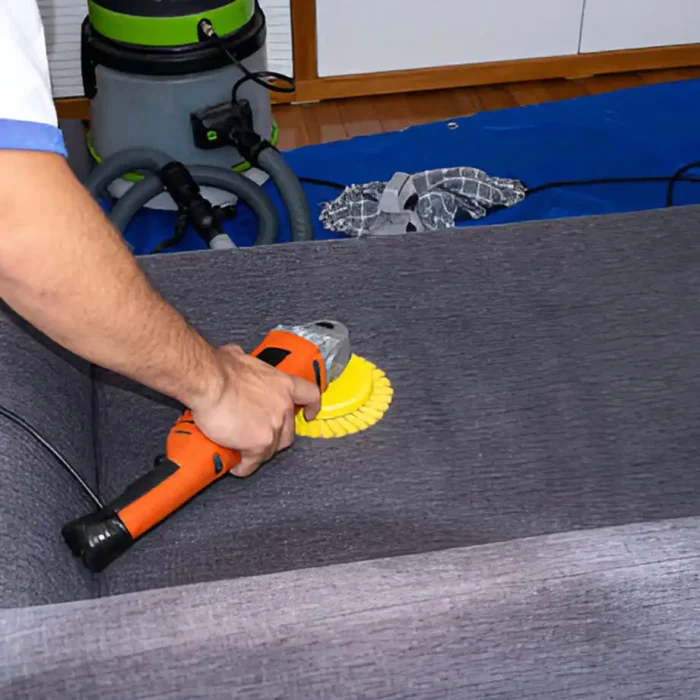 Reiniger, der das Sofa nach der Reinigung mit einer orangefarbenen Handschwabbelmaschine für eine gründliche Reinigung bearbeitet in Reichenbach im Vogtland