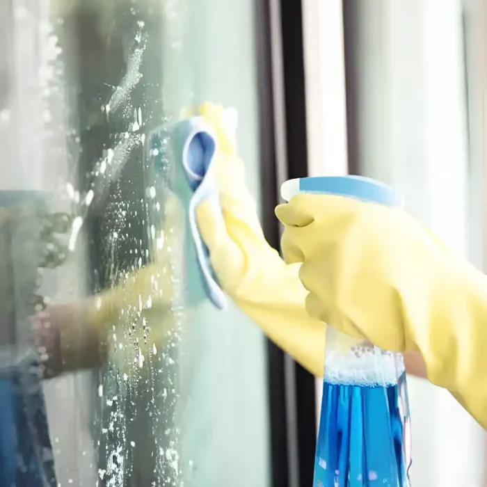 Hände in gelben Handschuhen reinigen ein Fenster mit blauem Spray in Einbeck
