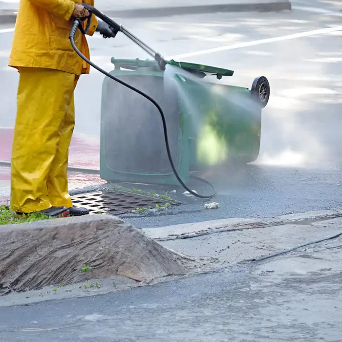 Arbeiter in gelber Regenkleidung wäscht einen umgestürzten Mülleimer auf dem Bürgersteig
