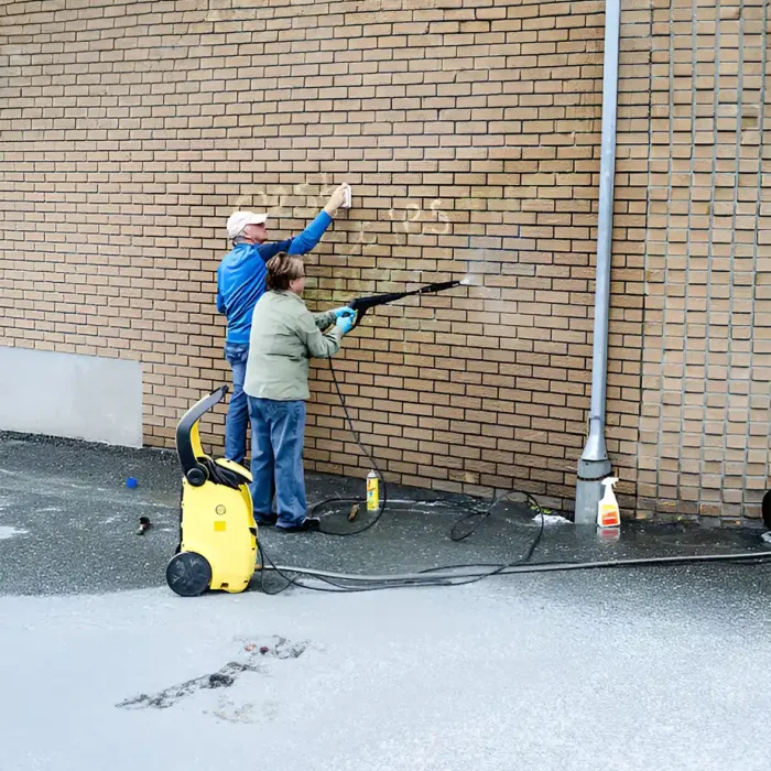 Zwei Personen säubern mit einem Hochdruckreiniger eine Backsteinmauer von Graffiti in Albstadt