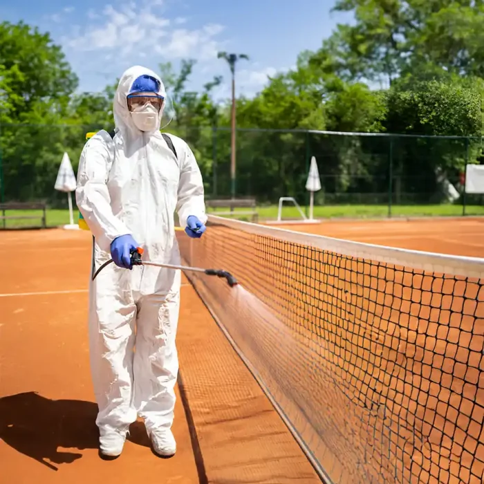 Arbeiter im Schutzanzug sprüht Desinfektionsmittel auf ein Tennisplatznetz in Reutlingen