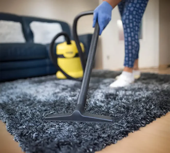 Person beim Staubsaugen eines Teppichs im Wohnzimmer mit einem Sofa im Hintergrund