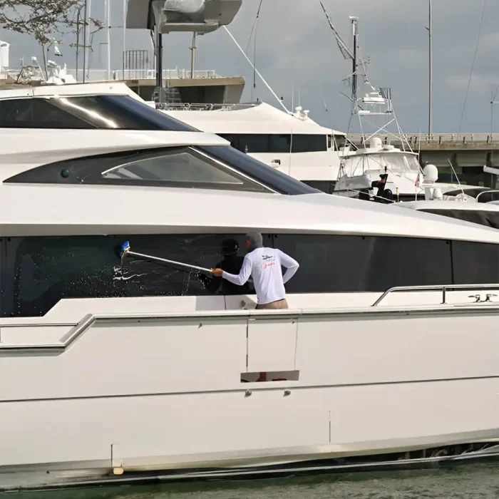 Person mit einer langen Bürste, um die Fenster einer Yacht im Hafen zu reinigen
