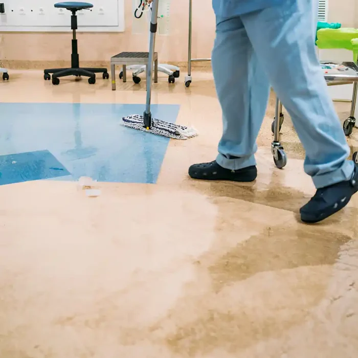 Person in blauen Kitteln wischt einen Fußboden in einer medizinischen Einrichtung, wobei im Hintergrund Geräte zu sehen sind in Friedberg